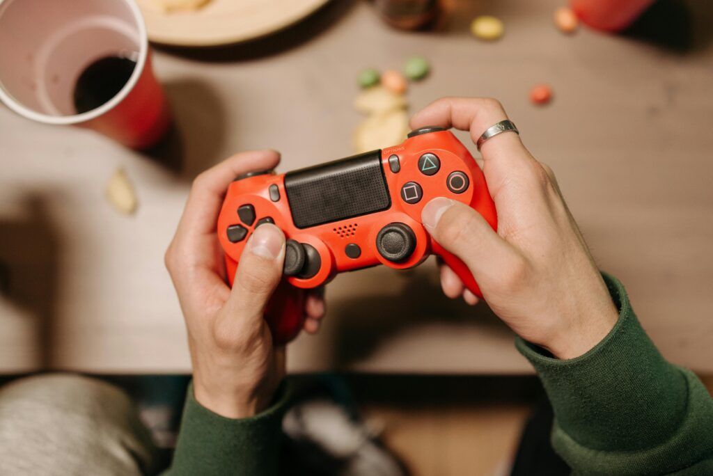 Person playing video games with a red controller at a desk.