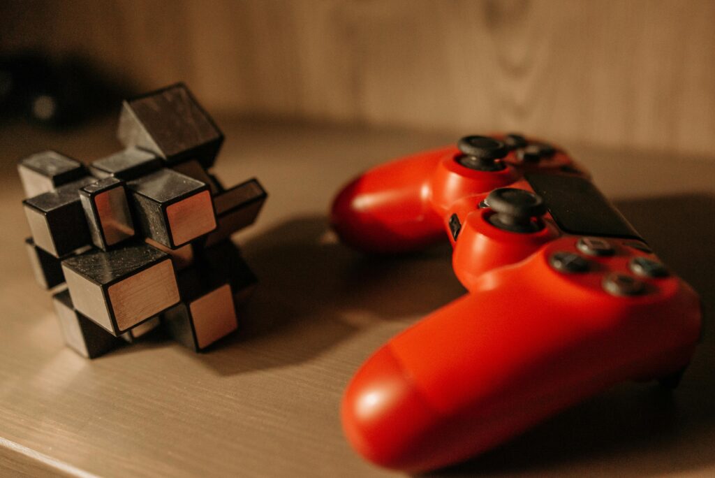 Close-up of a red game controller and 3D cube puzzle on a wooden surface.