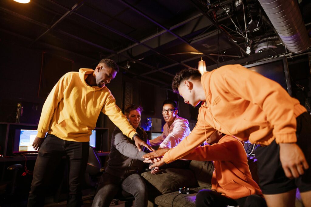 Group of diverse young gamers uniting in teamwork in a gaming room, celebrating victory.
